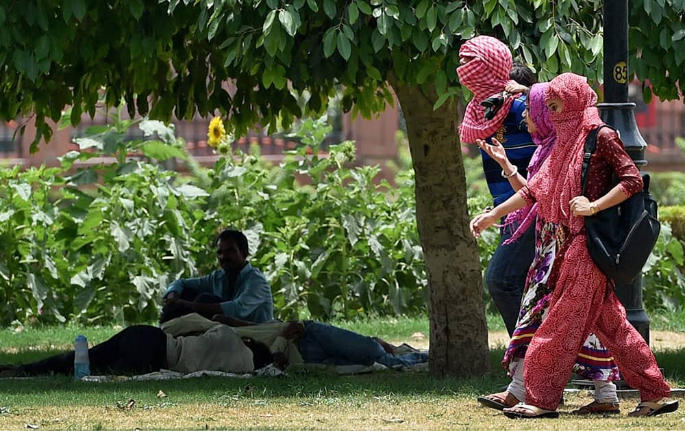 People walking with their heads covered while others take rest under a tree to get protection from scorching heat on a hot day in New Delhi.