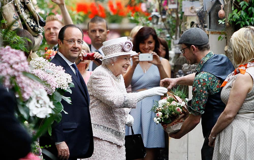 Britain`s Queen Elizabeth II, centre, and French President Francois Hollande, left, receive flowers during a visit at the Flowers Market (Marche aux Fleurs) in Paris.