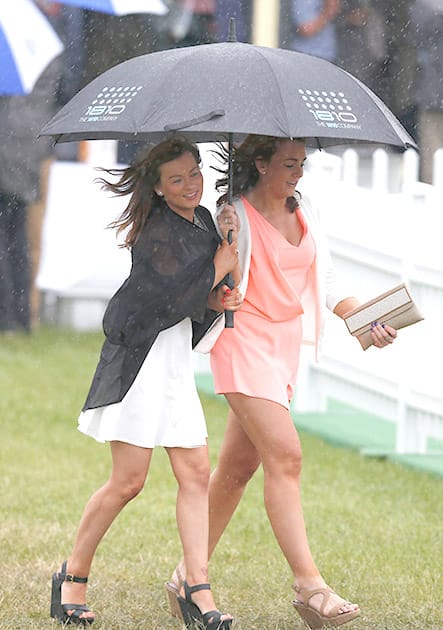 Race fans shelter from the rain underneath an umbrella as they wait for the Epsom Derby at Epsom racecourse, England.