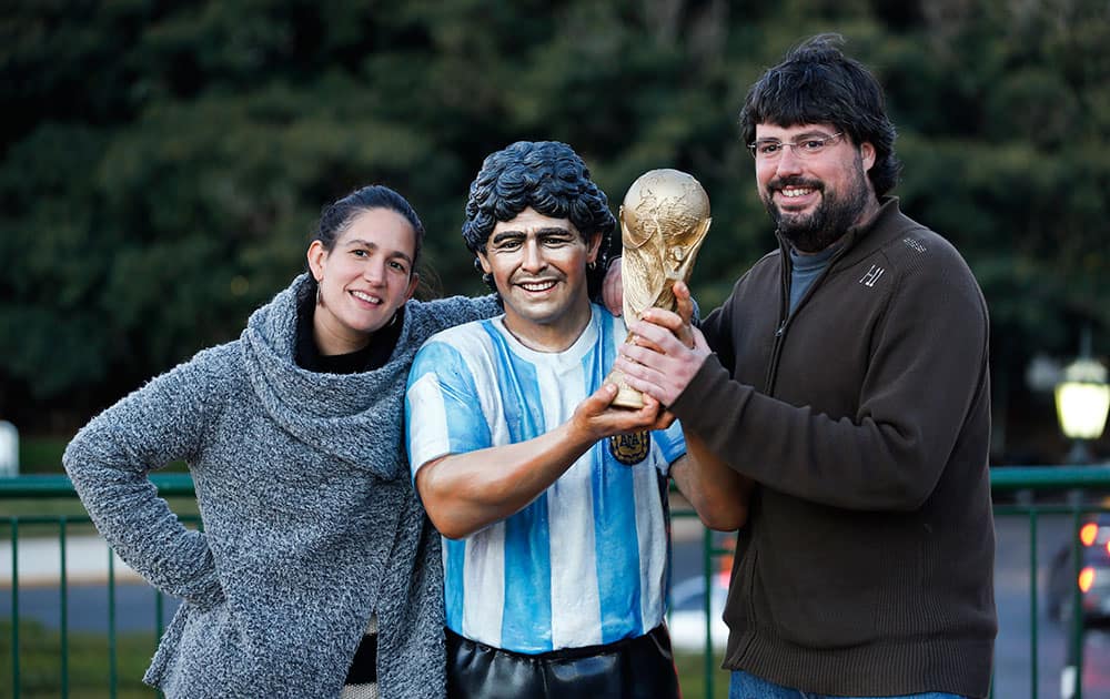 Two people pose for a picture with a statue resembling Argentine soccer star Diego Maradona holding the replica of a World Cup trophy, at a park in Buenos Aires.