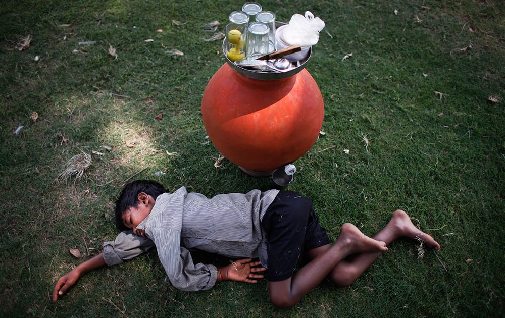 A boy, selling lemon water in an earthen pot, sleeps on the grass at a public park on a hot summer afternoon in New Delhi.