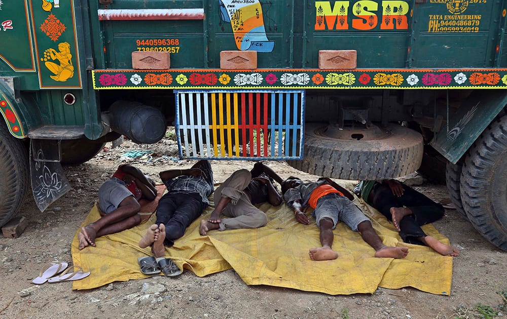 Laborer rests under a truck at a roadside on a hot summer day in Hyderabad.