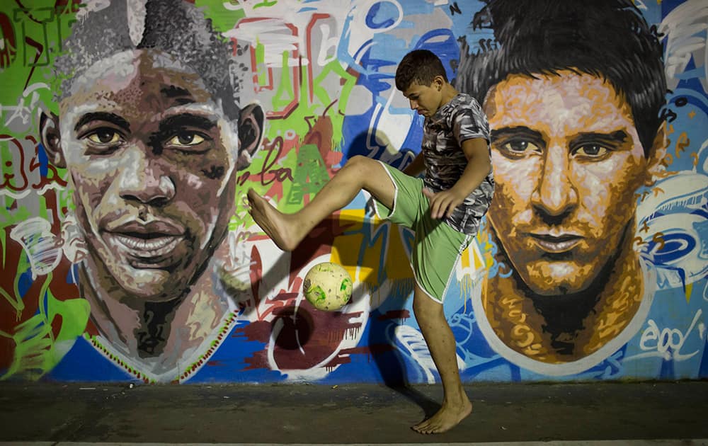 A boy practices freestyle soccer next to a mural depicting soccer players Italy`s Mario Balotelli and Argentina`s Lionel Messi at a slum in Rio de Janeiro, Brazil.