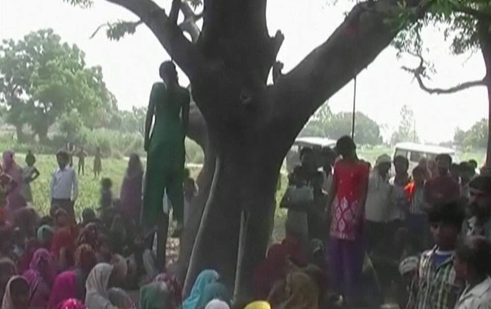 Villagers sit in silent protest under the bodies of two teenage sisters hanging from a tree in Katra village in Uttar Pradesh state.