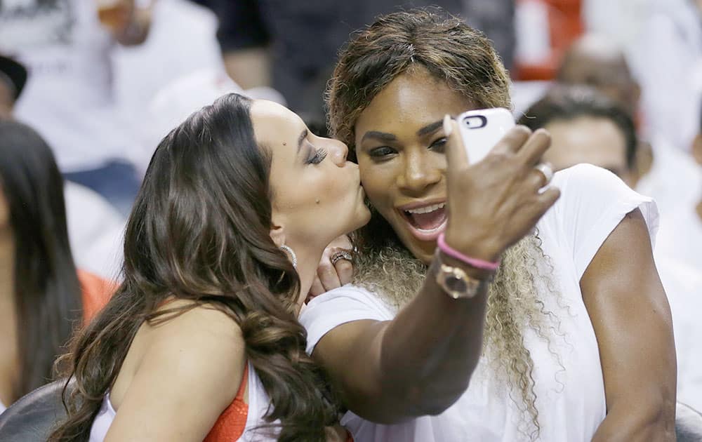 Adrienne Bosh, left, wife of Miami Heat player Chris Bosh, kisses tennis player Serena Williams as Willians takes a photo during the first half Game 6 in the NBA basketball playoffs Eastern Conference finals between the Indiana Pacers and the Heat.