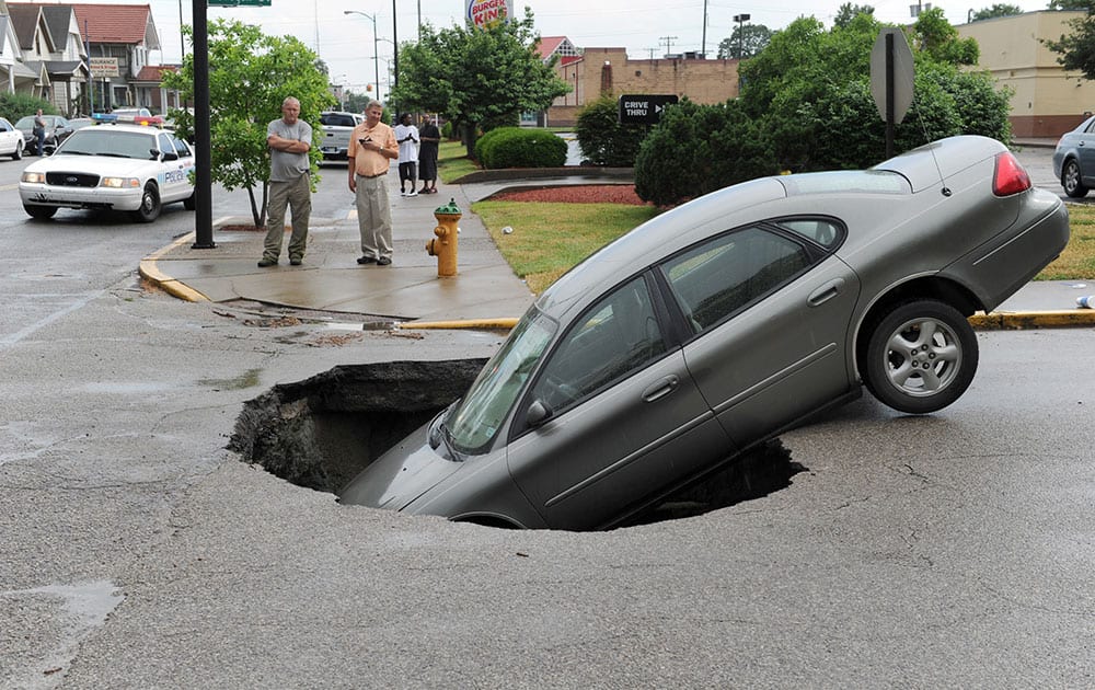 A car rests in a hole after a water main broke on Oregon St. at Main St. in Evansville, Ind.