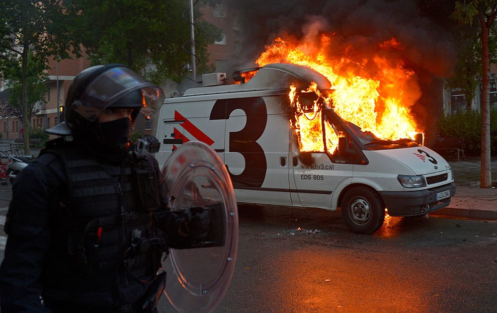 A riot police walks in front of a burning mobile van unit for TV during a protest against the eviction of squatters from a building in Barcelona, Spain.