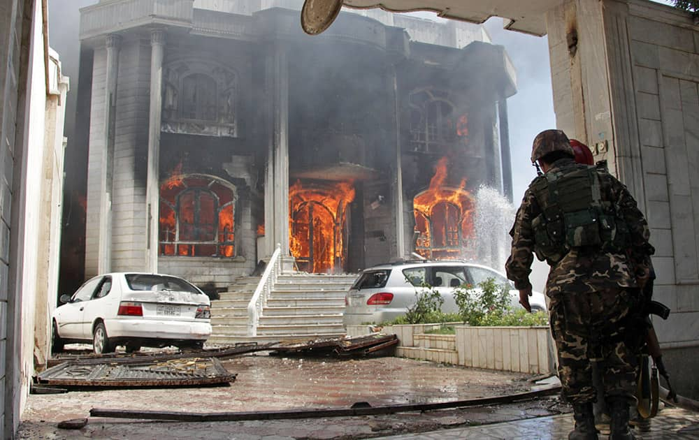 Afghan security forces watch a house burn at the site of a clash between insurgents and security forces at the Indian Consulate in Herat, Afghanistan.