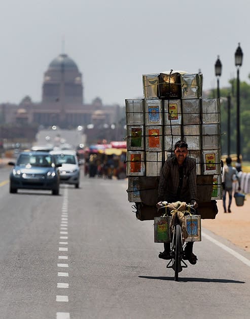 A man carries tin-containers on a bicycle at Rajpath on a hot day in New Delhi.