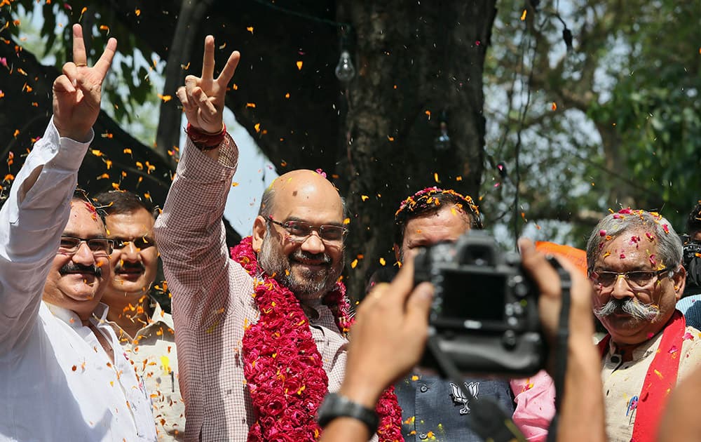 Bharatiya Janata Party (BJP) leader Amit Shah, wearing garland, displays the victory symbol as he celebrates with party supporters outside the BJP party in New Delhi