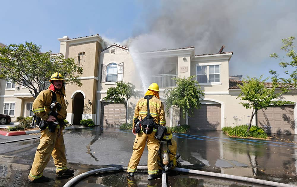 Firefighters pour water on a condominium complex that was caught in the path of a wildfire in Carlsbad, Calif.