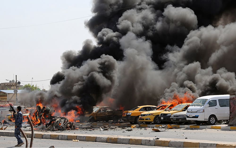 An Iraqi policeman stands near burning vehicles moments after one in a series of bombs hit the Shiite stronghold of Sadr City, in Baghdad, Iraq.