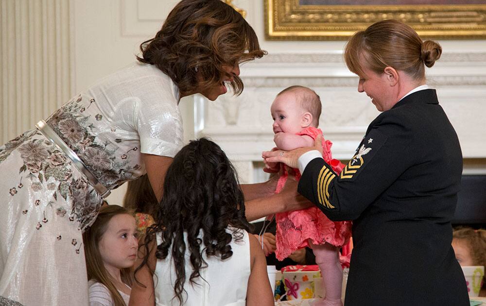 First lady Michelle Obama reaches for Avery Noelle Brindley as she visits a crafts table during the annual Mother’s Day Tea to honor military mothers, at White House in Washington, hosted by the first lady and Jill Biden.