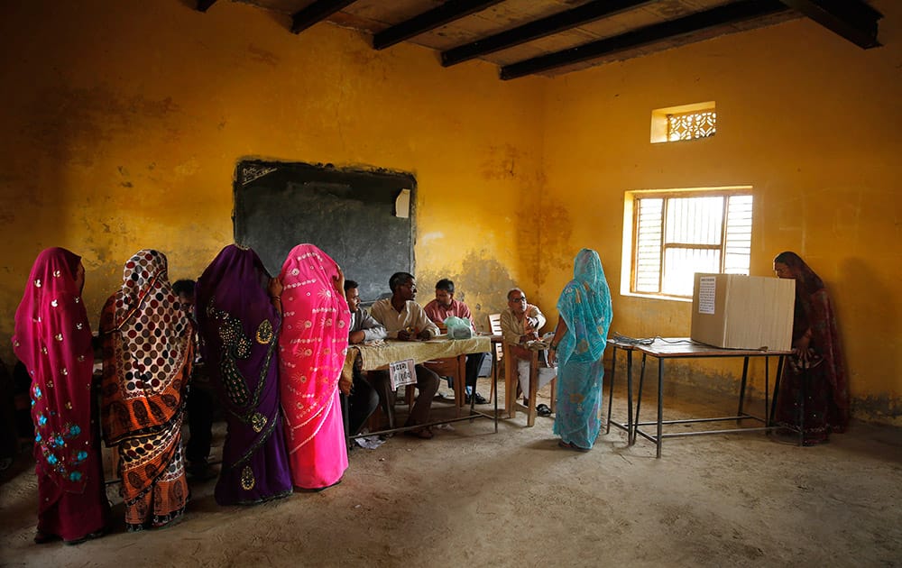 Rural Hindu women with their faces covered wait in a queue as another woman casts her vote on the final day of polling in Kunwarpur village, about 40 kilometers (25 miles) northwest of Jaunpur district, in the northern Indian state of Uttar Pradesh.