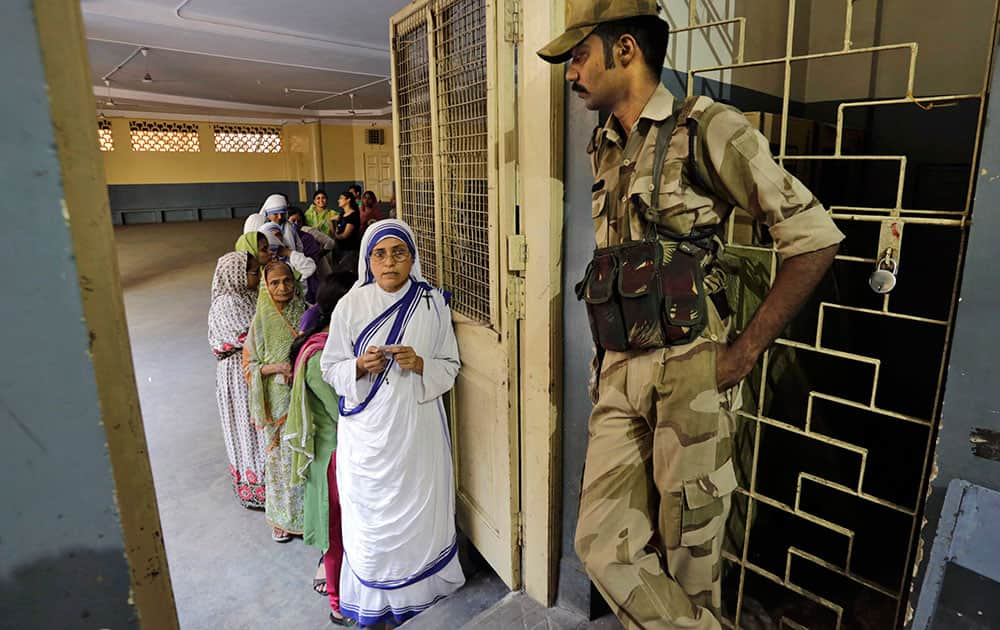 A nun waits in queue with others to cast her vote as a security officer stands watch at a polling station in Kolkata.