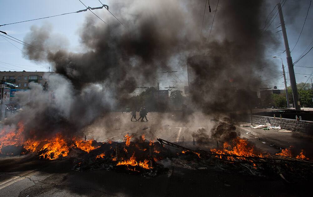 People walk through a square as black smoke billows from burning tires, to prevent government troop`s armored personnel carriers passing through, in the center of Mariupol, eastern Ukraine.