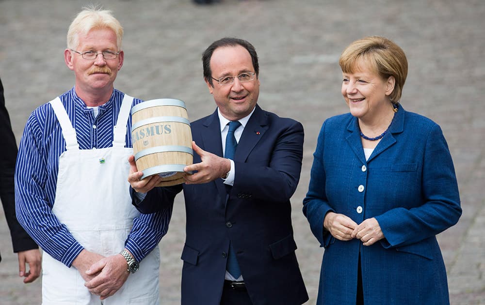 French President Francois Hollande, center, next to German Chancellor Angela Merkel, right, receives a barrel of pickled herring from fisherman Henry Rasmus, left, after their walk through the old town of Stralsund, northern Germany.