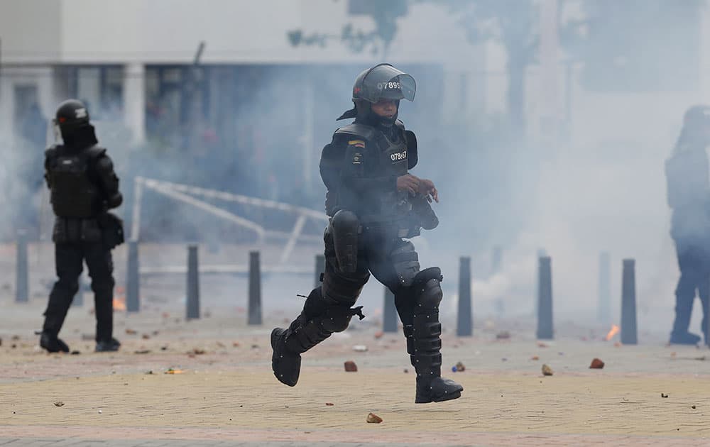 A riot police officer runs to get more tear gas during confrontations with students who gathered outside the Universidad Nacional in Bogota, to show their support for the ongoing nationwide agrarian strikes, in Bogota, Colombia.