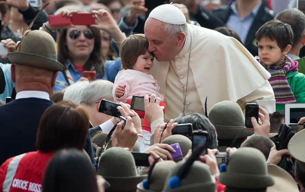 Pope Francis kisses a child as he arrives for his weekly general audience in St. Peter`s Square at the Vatican.