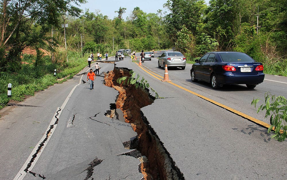 Motorists make their way through as people examine a cracked road after an earthquake in Chiang Rai province, northern Thailand.