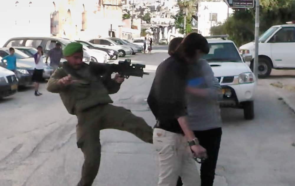 In this image taken from video obtained from Youth Against Settlements, a group of Palestinian activists, which has been authenticated based on its contents and other AP reporting, an Israeli soldier kicks at Palestinian teens in the West Bank city of Hebron. 