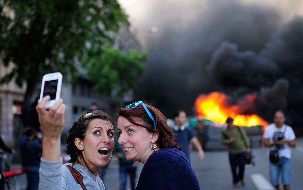 Tourists take a `selfie` picture as demonstrators burn a trash container during a May Day rally in Barcelona, Spain. Tens of thousands of workers marked May Day in European cities with a mix of anger and gloom over austerity measures imposed by leaders trying to contain the eurozone`s intractable debt crisis. 