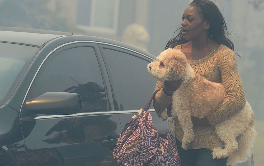 A woman who is evacuating her home carries a dog to a vehicle in smoke from the Etiwanda Fire in Rancho Cucamonga, Calif.