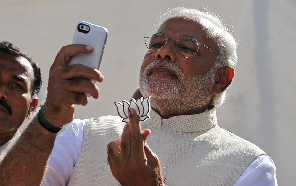 Bharatiya Janata Party’s prime ministerial candidate Narendra Modi holds his party’s symbol and looks into his phone after casting his vote in Ahmedabad.