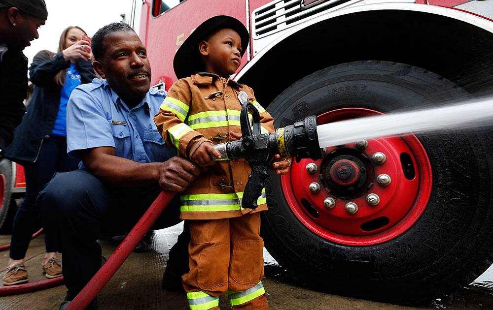 Tyren Johnson, 3, of Detroit, shoots a fire hose with the help of Sgt. Reginald Harper during his wish to be a fireman at Detroit Fire Department Engine 54 in Detroit. Make-A-Wish Michigan is celebrating World Wish Day by granting Johnson, who had a heart transplant, his wish. 