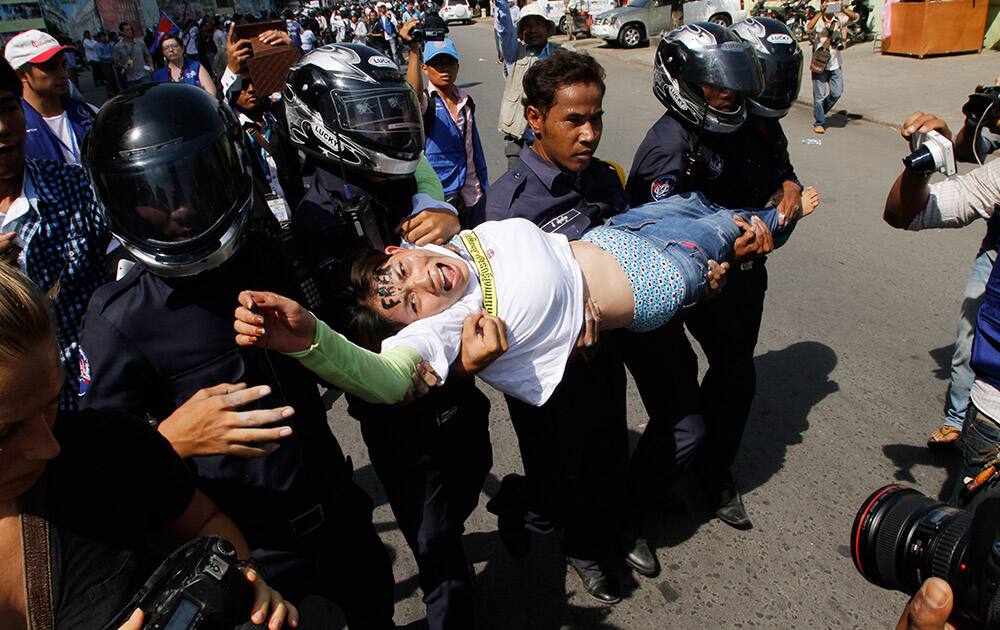 A supporter, center, from Boeung Kak Lake community is carried by local security guards near a blocked main street near the Phnom Penh Municipality Court during villagers` gathering to call for the release of anti-governments protesters who were arrested in a police crackdown, in Phnom Penh, Cambodia.