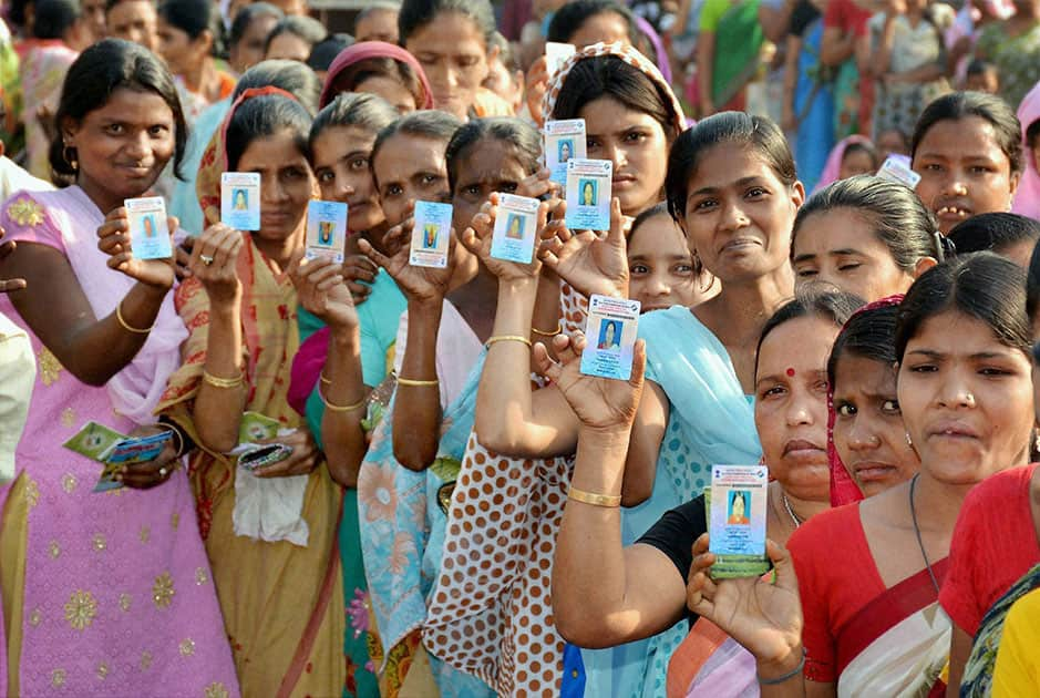 Woman voters show their voter identity cards as they wait in a queue to cast votes for Lok Sabha polls outside a polling station, in Guwahati.