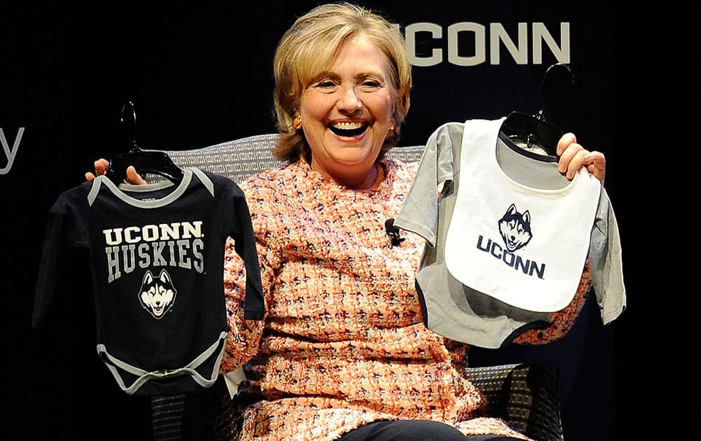 Former Secretary of State Hillary Rodham Clinton holds up UConn Huskies outfits given to her by university president Susan Herbst for Clinton`s future grandchild at the end of a speaking appearance at the Edmund Fusco Contemporary Issues Forum at the University of Connecticut, in Storrs, Conn. 