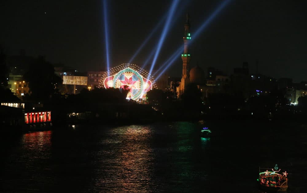 A pleasure boat travels down the darkened Nile as a lit-up venue hosting a concert shines in the background near a mosque in Cairo, Egypt.