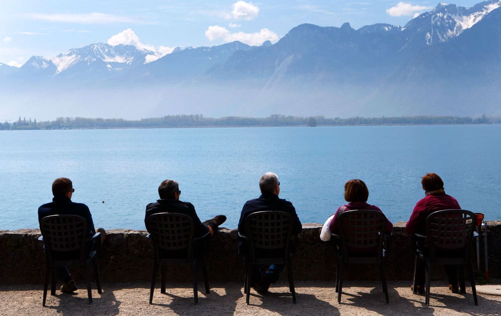 People enjoy the sunshine on the bank of the lake of Geneva in front of the Swiss Alps near the Chateau de Chillon (Chillon Castle) in Veytaux near Montreux, Switzerland.