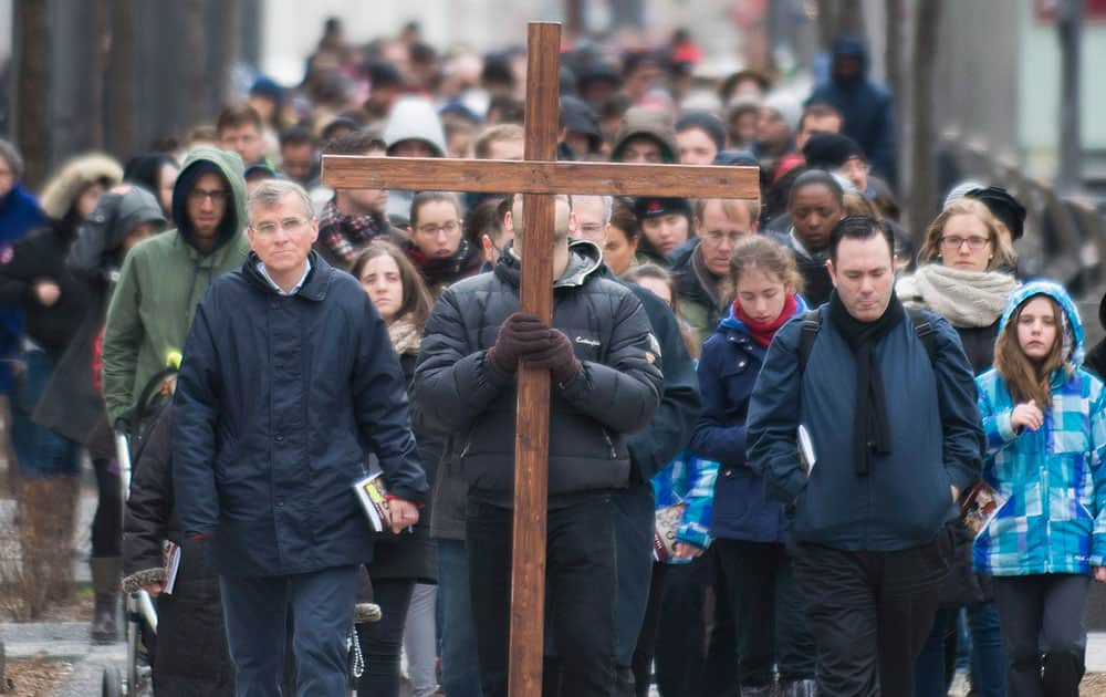 A man walks with a crucifix along with the faithful as they participate in the Way of the Cross on Good Friday in Montreal.