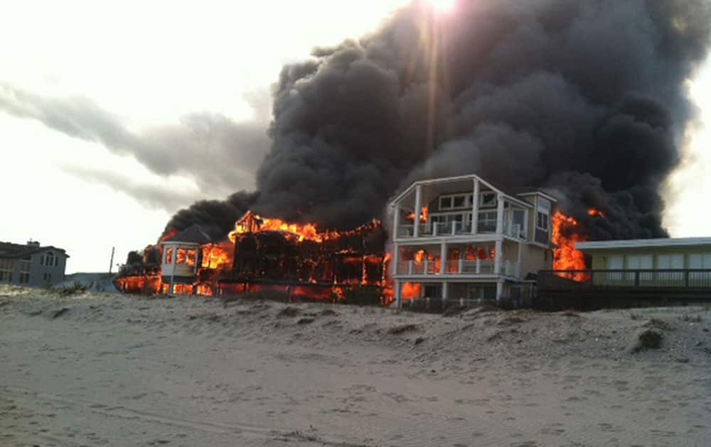 In this photo provided by Joanne Dollarton, fire engulfs three homes near the beachfront, in Sea Isle City, N.J. Authorities say no injuries have been reported in the smoky fire, which erupted around 4:30 p.m. Friday and sent large clouds of black smoke spewing across the region.