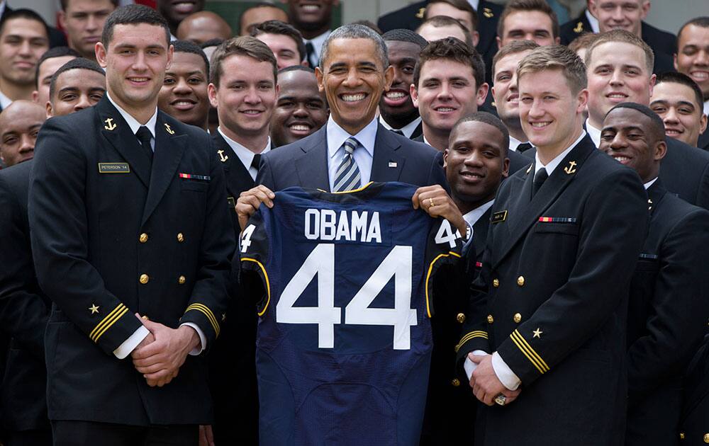 Holding his new Navy football jersey, President Barack Obama stands between Navy football team co-captains Matt Aiken right, and Cody Peterson, left, for photographs during a ceremony in the Rose Garden of the White House in Washington.