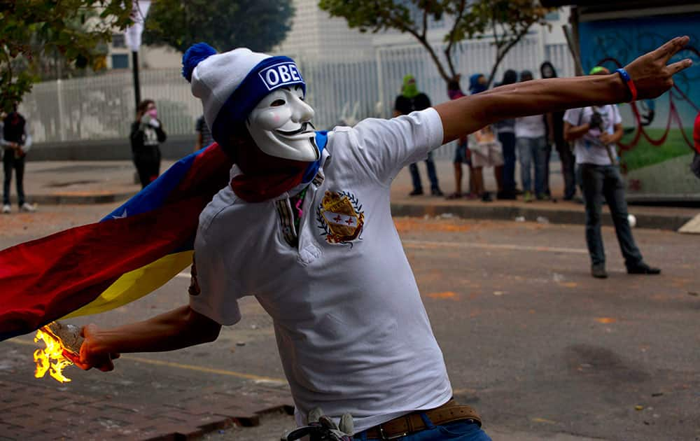 An anti-government protester wearing a Guy Fawkes mask throws a molotov cocktail at the Bolivarian National Police during clashes in Caracas, Venezuela.