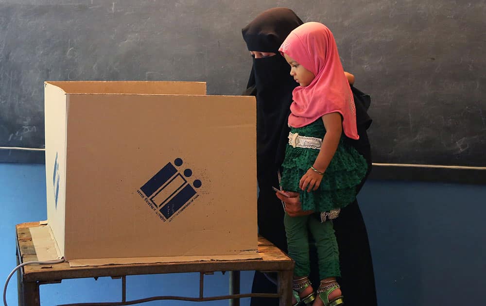 A veiled woman holds her daughter as she casts her vote at a polling station set up inside a school in Bangalore.