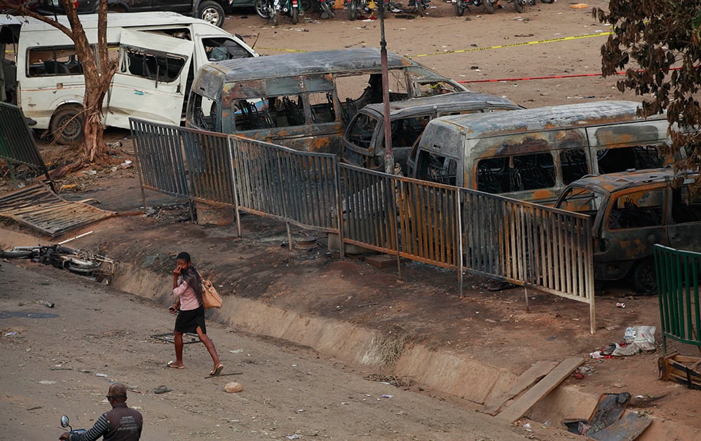 A woman walk past burnt out buses at the scene of an explosion at a bus park in Abuja, Nigeria.