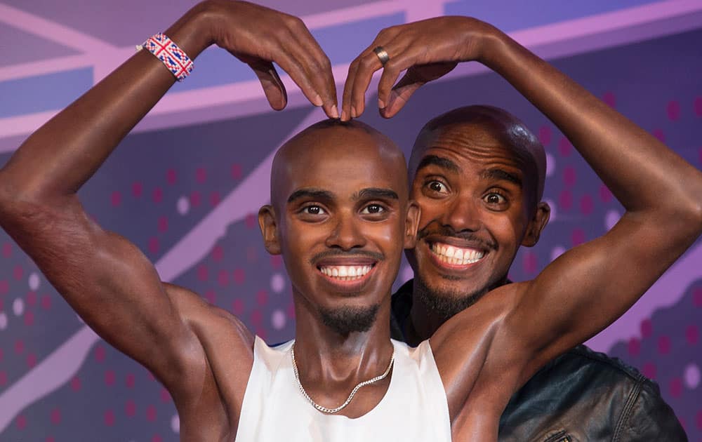 British Athlete Mo Farah, left, peers through the arms of one of the two wax figures created in his likeness, during a photo call at Madame Tussauds in central London.