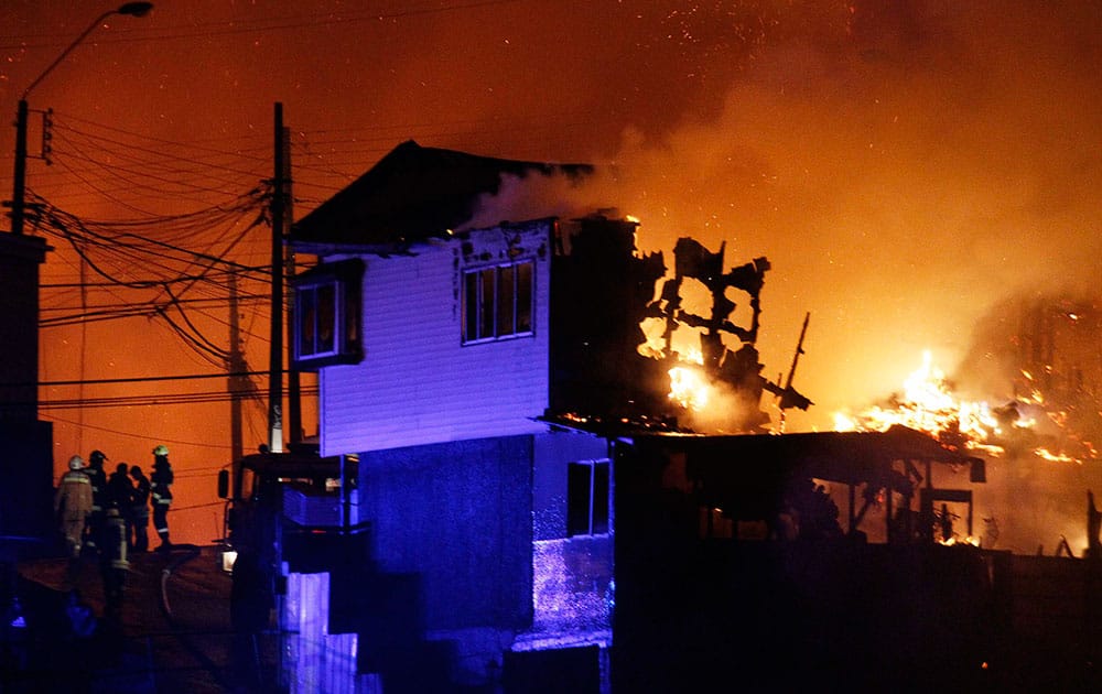 A group of firefighters stand next to burning homes as a forest fire rages towards urban areas in the city of Valparaiso, Chile. Authorities say the first fire has destroyed at least 150 homes and is forcing evacuations.