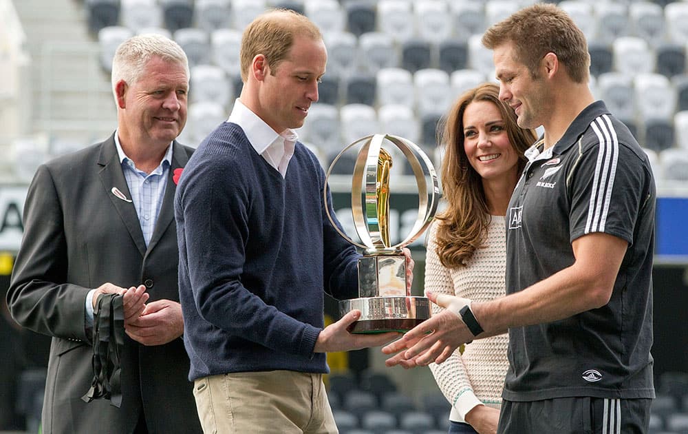 Watched by NZ Rugby CEO Steve Tew, left, Britain`s Prince William hands over the IRB Junior World Championship Trophy to All Blacks captain Richie McCaw, right, as his wife Kate, the Duchess of Cambridge, second from right, watches during their visit to a young players’ rugby tournament, at Forsyth Barr Stadium, in Dunedin, New Zealand.