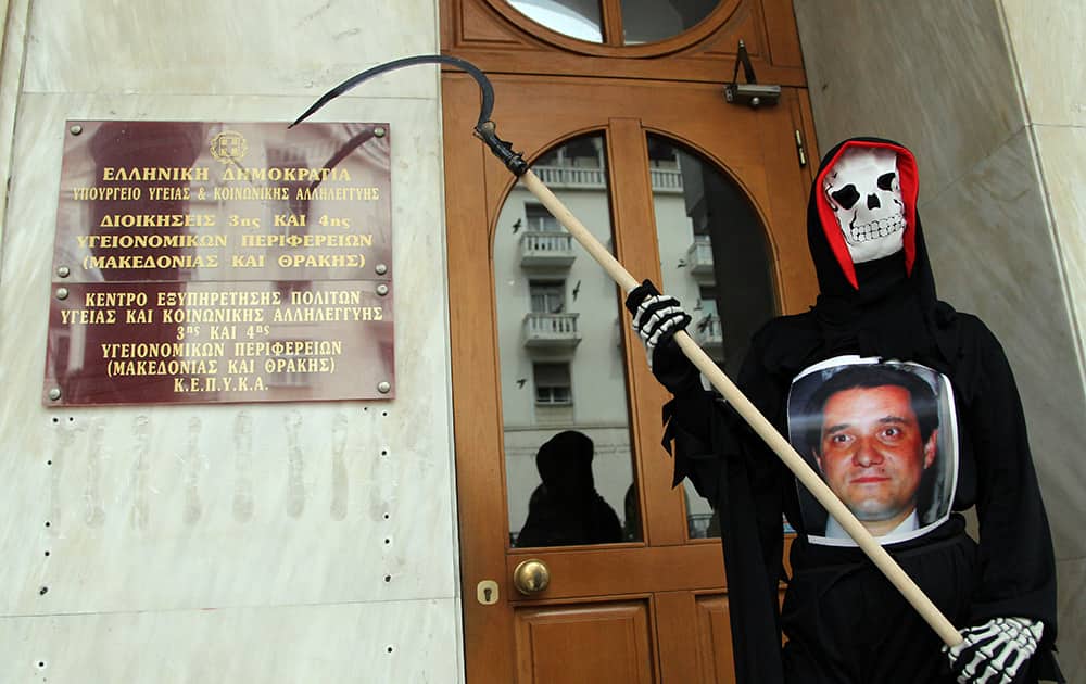 A protester dressed as the grim reaper, and wearing a photo of Health Minister Adonis Georgiadis, stands outside a government health office, in the northern Greek city of Thessaloniki.