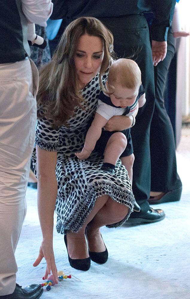 Britain`s Kate, the Duchess of Cambridge, holds Prince George and picks up a toy that the prince dropped during a visit to Plunket nurse and parents group at Government House in Wellington.