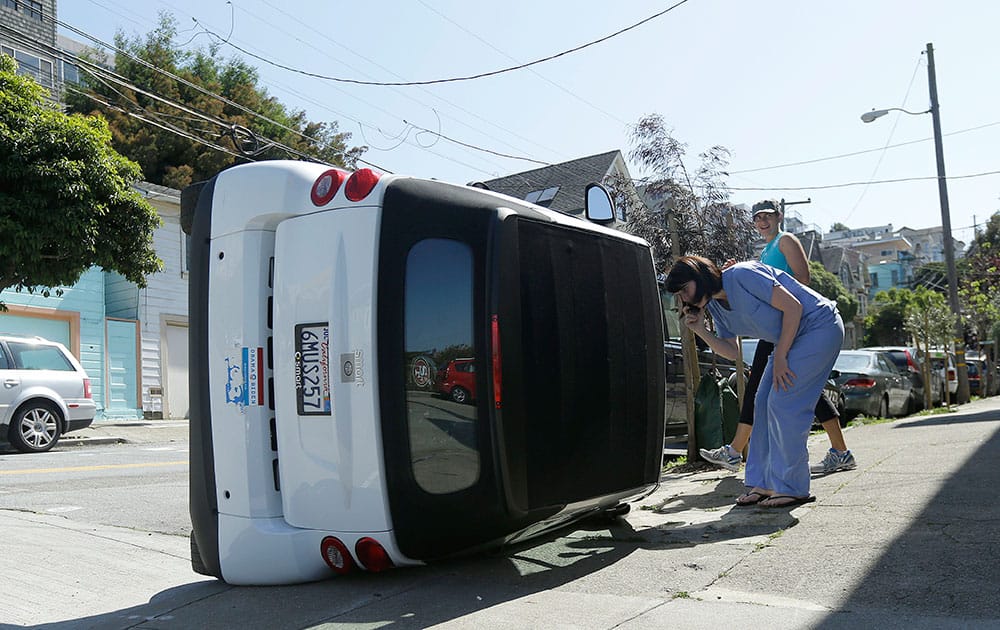 Shelley Gallivan, foreground right, looks into a tipped over Smart car which belongs to her friend on the corner of Prospect and Oso streets in San Francisco.