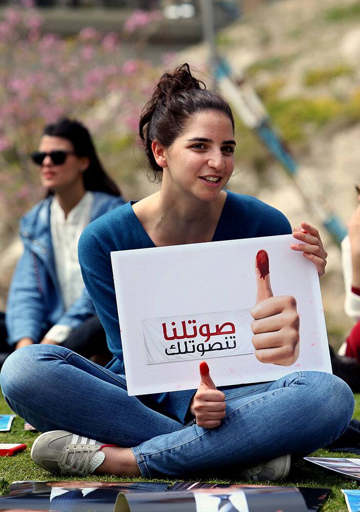 A Lebanese activist holds a placard with Arabic that reads,` vote for us so that we vote for you,` during a protest in downtown Beirut, Lebanon.