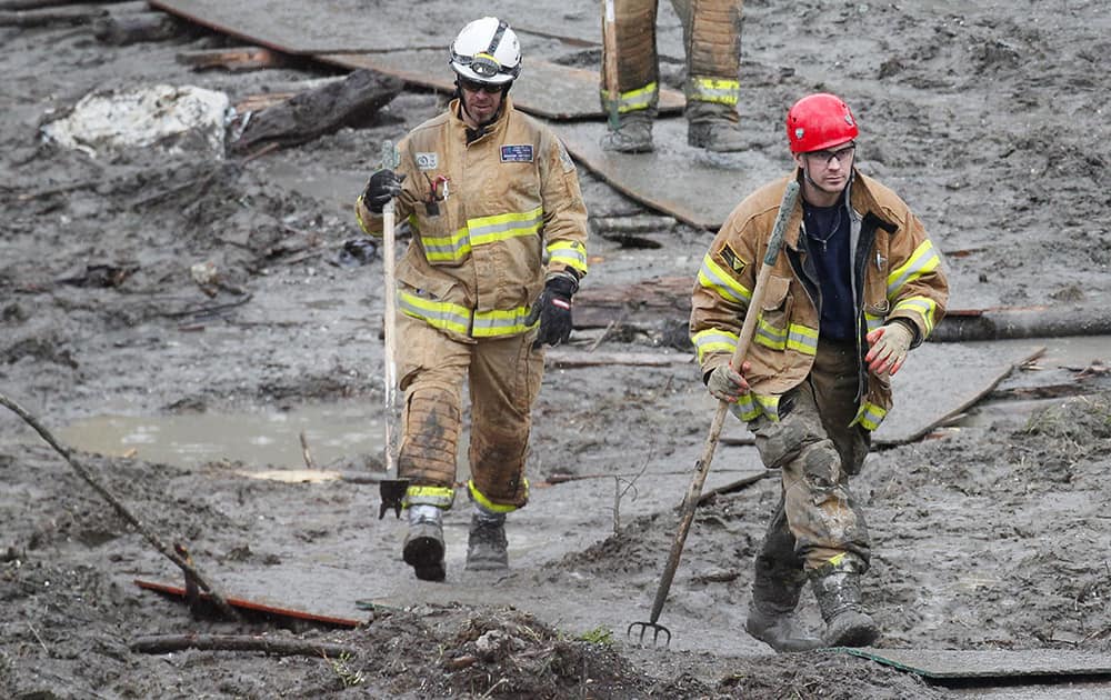 Snohomish County firefighters walk through the mud on a plywood path at the west side of the mudslide on Highway 530 near mile marker 37 in Arlington, Wash.