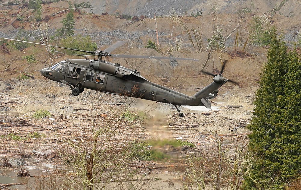A military helicopter flies, over mud and debris from the massive mudslide that struck Saturday near Darrington, Wash. Search and recovery work continued throughout the day.