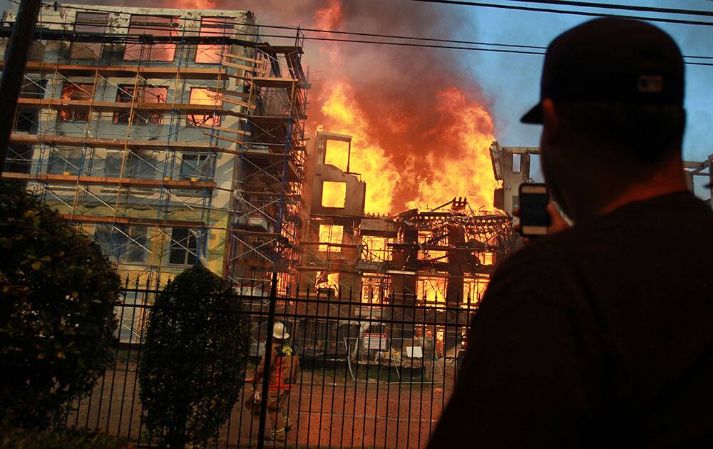 A man views a five-alarm fire that ignited inside an apartment construction site at the corner of Marconi Street and Dallas Avenue.